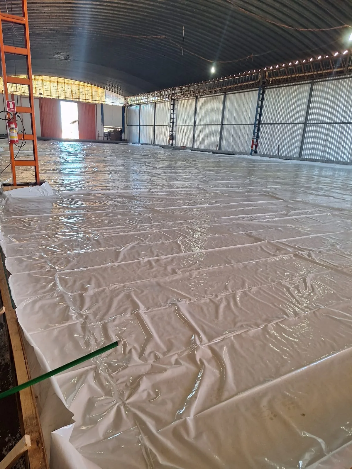 Lona plástica estendida sobre a base preparada, dentro do galpão, antes da concretagem